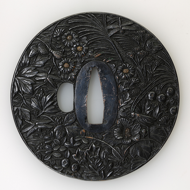 素材 赤銅色揚地
形　丸形
櫃孔　片櫃孔
技法 鋤出高彫　色絵　鋤残耳 

特徴 日本特有の合金である赤銅は、銅に金を加えたものです。坩堝の中で溶融する際に熱する木炭の良否も出来上がりの品質に影響したといいます。
本作は、この上質な地金に濃密な秋草に虫図を彫り、色深く色揚げが施された鐔です。手にするとずっしりと重さが伝わります。

春親(はるちか)は、浜野氏、奈良派、土屋氏、鈴木氏などに同銘が複数存在します。
