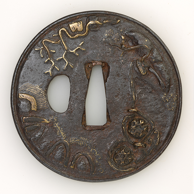 素材 鉄 真鍮
形　丸
櫃孔　片櫃孔
技法 鋤残耳　象嵌 色絵

特徴 厚みがあり堅牢な鐔。真鍮象嵌で何やら重々しい石材風の塊や複雑な縄・枯れ木の形状を丸い鐔の輪郭に沿って流転するように配置。それらの間を雑草が生い茂る風景は、生と死が交錯する異空間、京都化野(あだしの)のような場所に着想をえていると鑑せられます。

状態　良好です。